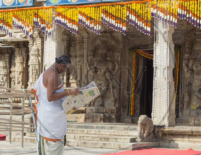A Hindu Priest is seen engrossed in reading a Morning Newspaper inside the Shiva temple in Talakadu village near Mysuru in India.
