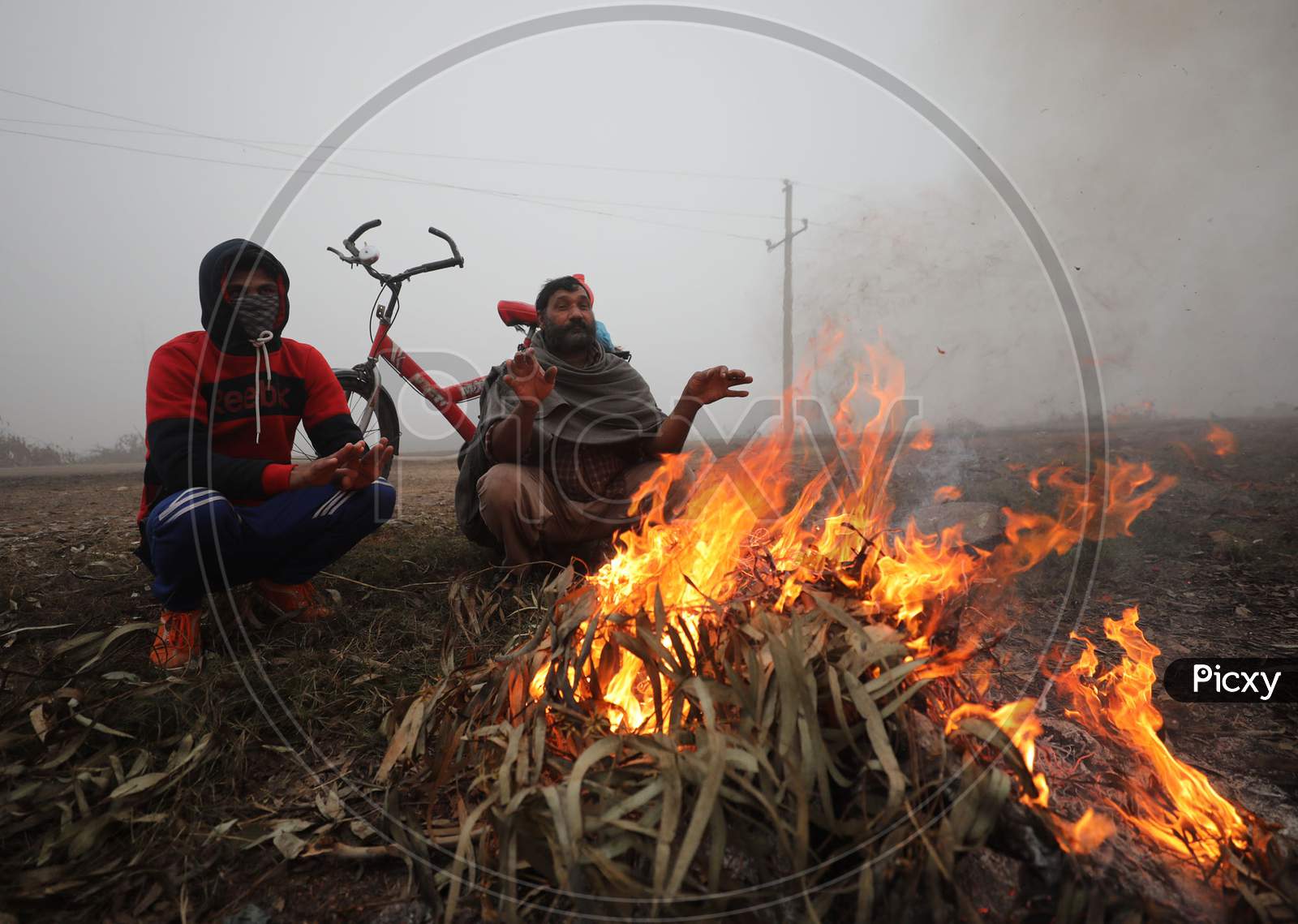 People warm themselves as they sit near the bone fire in a chilli and foggy morning in Jammu,27 Dec,2020.