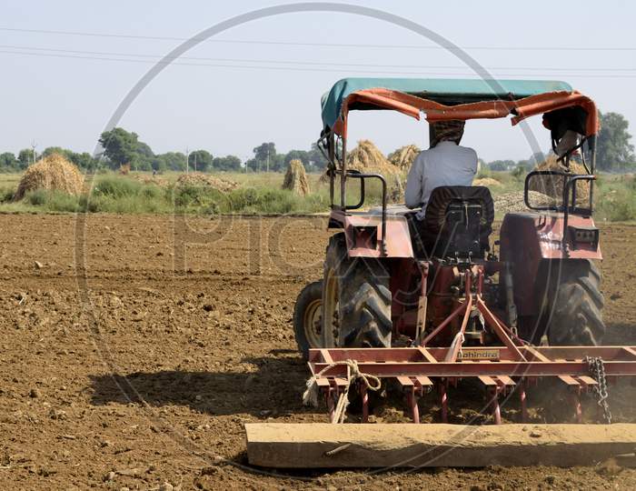 A Indian Farmer Is Cultivation A Field With His Tractor, Making It Ready To Sow The Seeds