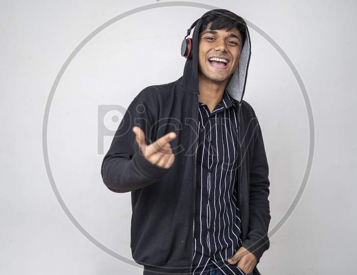 Young Handsome Man Listening Music With Headphones Wearing A Black Hoodie One Hand In A Pocket Standing On White Background