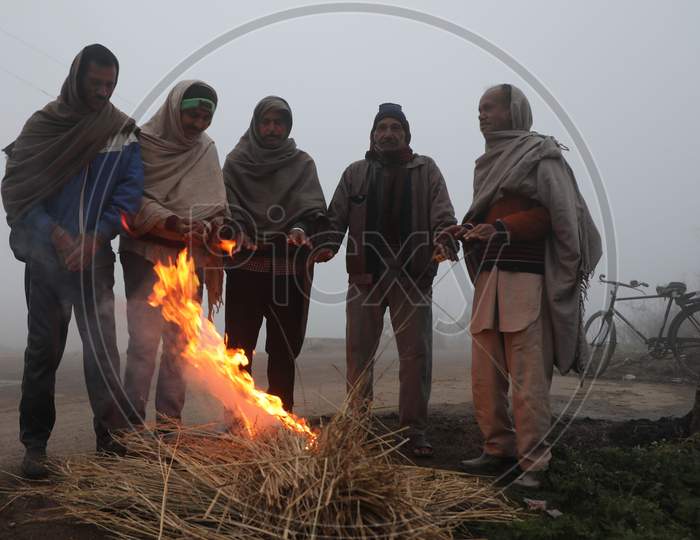 People warm themselves as they sit near the bone fire in a chilli and foggy morning in Jammu,27 Dec,2020.
