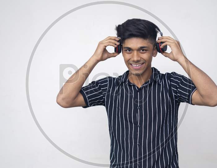 Happy Young Indian Man In Half Shirt, Holding Wireless Headphone With Both And Listening Music.