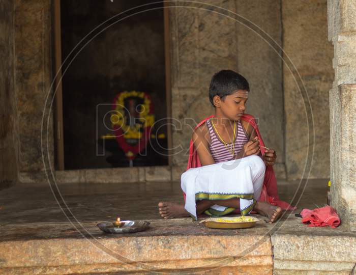 An Young Priest is seen sitting outside a Hindu Shiva temple with Flowers and Holy water to be distributed to the devotees.