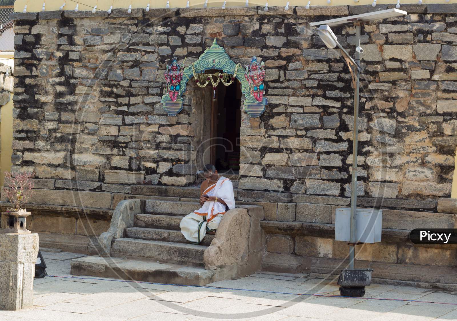 A Beautiful picture of an Hindu Priest seen immersed in browsing his smartphone outside the Shiva temple in Talakadu village near Mysuru,India.