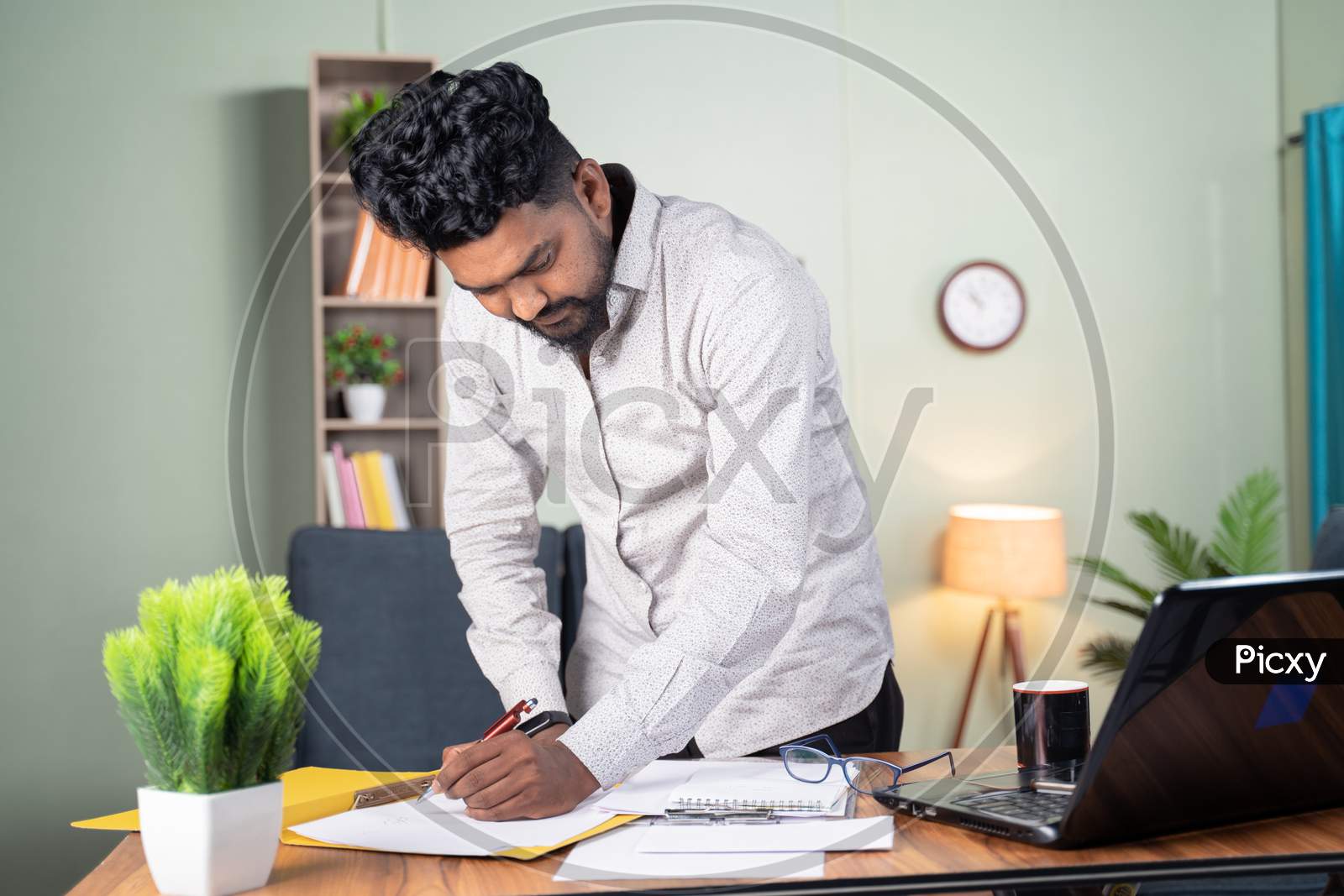 Young Business Man Busy In Paperwork By Referring Documents And Laptop - Concept Of Preparing Plan, Managing Tasks By Standing At Office Table.
