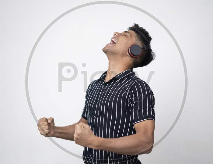 Young Indian Handsome Man In Headphone Gesturing And Keeping Mouth Open While Standing Against White Background .Enjoying Music And Closed Eyes.