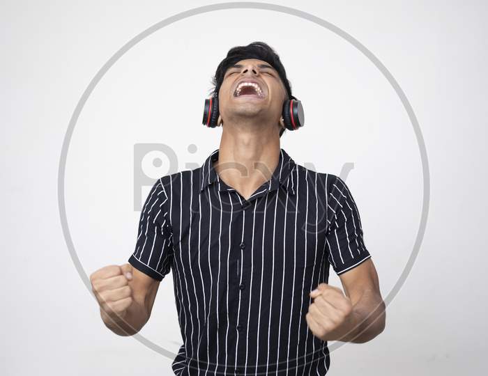 Young Indian Handsome Man In Headphone Gesturing And Keeping Mouth Open While Standing Against White Background .