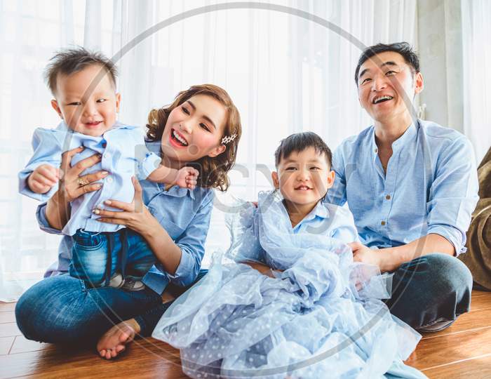 Happy Asian Family Smile And Laugh Together In Living Room At Home. Two Parents And Two Children Kids. People Lifestyle In State Quarantine After Travel On Covid-19 Or Coronavirus Epidemic Concept