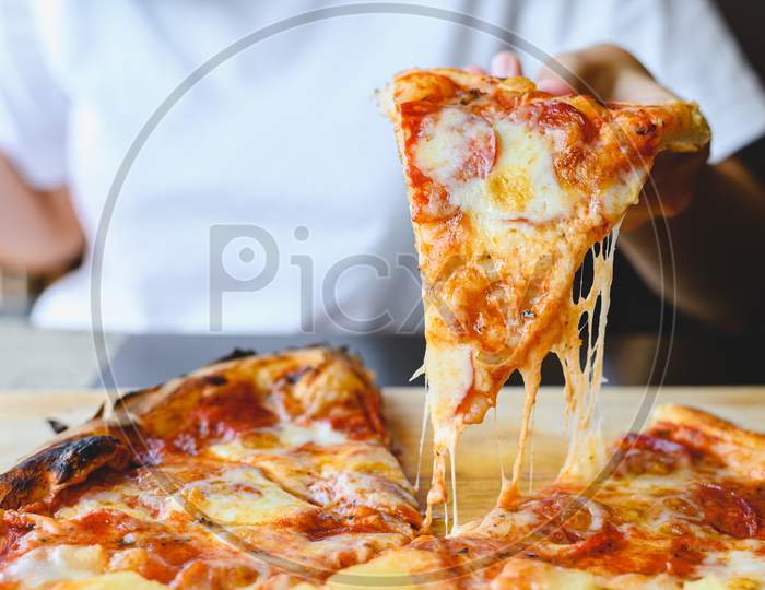 Wood Fire Cheesy Pizza Slice In Hand. Traditional Hawaiian And Salami Pizza Savory Dish Flavour Of Origin Italian Restaurant. Wood-Fired Oven Pizza With People Holding Pizza Background