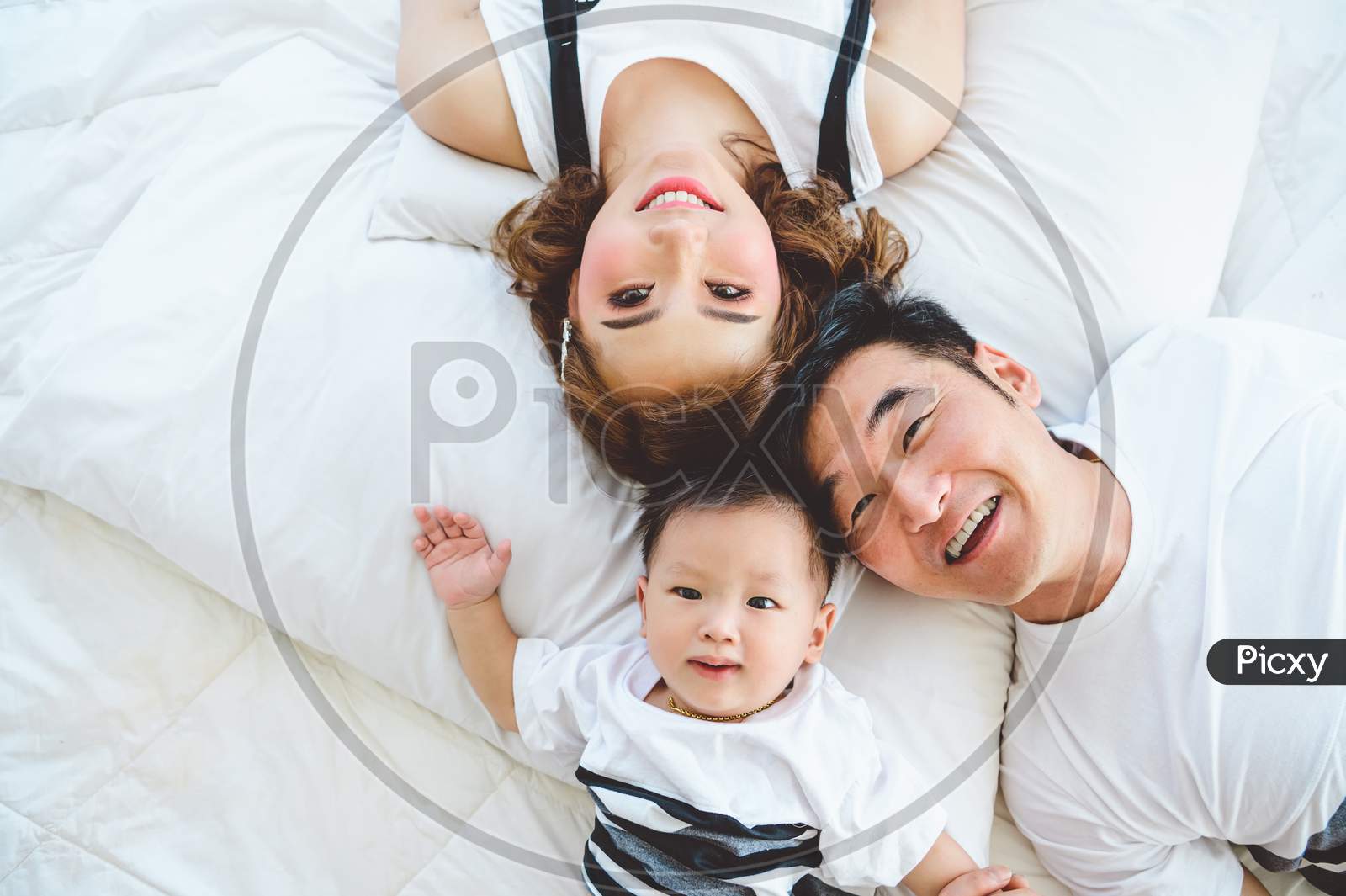 Top View Of Asian Family With Father Mother And Son On White Pillow Bed In Bedroom At Home. Happy Parents And Child Baby Concept. People Lifestyle In State Quarantine From Covid-19 Or Coronavirus