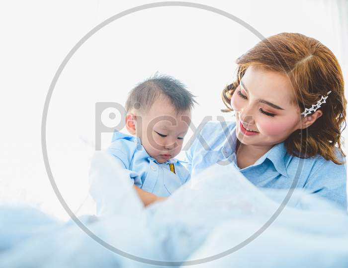 Asian Mother And Her Son Wearing Blue Shirts On Bed In Bedroom With Copy Space At Home. People Lifestyle And Newborn Medical Concept. State Quarantine In Covid-19 Or Coranavirus Epidemic Theme