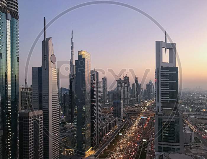 Beautiful Sunset View With Purple Sky To Futuristic City Infrastructure And Skylines Buildings. Cars Moving On Highway With Lights. Dubai, United Arab Emirates