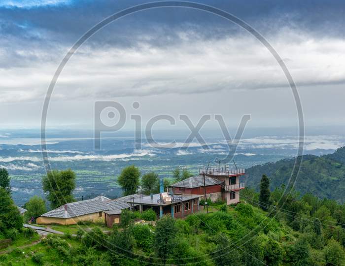Building Perched On The Edge Of A Mountain With Trees All Around Looking Over A Beautiful Vista Landscape Of A Valley Covered In Clouds At Dawn Shot In Mcleodganj Of Dharamshala Valley In Himachal Pradesh In India A Popular Tourist And Homestay Destination
