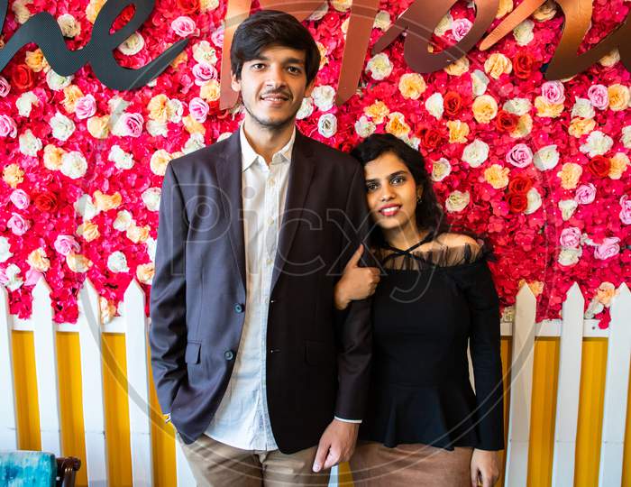 Portrait Of Young Happy Indian Couple In Love Standing Against Floral Background, Boyfriend Girlfriend Relationship, New Year Or Valentines Day.