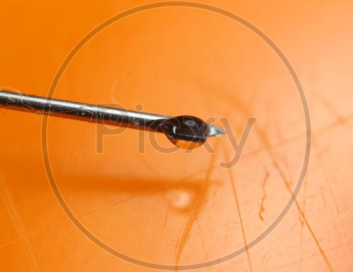 Water Drop Falling From The Syringe Needle Against Orange Background