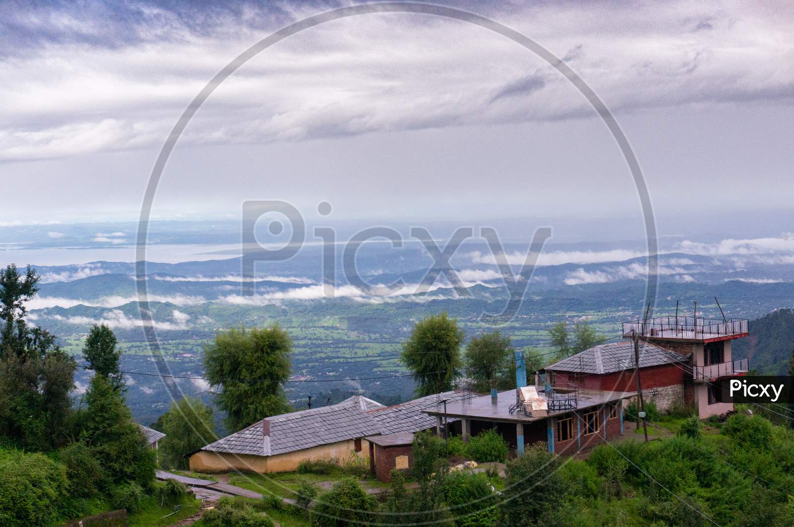 Building Perched On The Edge Of A Mountain With Trees All Around Looking Over A Beautiful Vista Landscape Of A Valley Covered In Clouds At Dawn Shot In Mcleodganj Of Dharamshala Valley In Himachal Pradesh In India A Popular Tourist And Homestay Destination