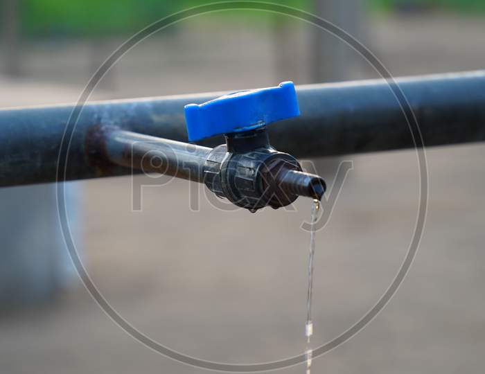 Selective Focus On Water Dropping From Blue Water Tap. Regular Flowing Water From Blue Faucet. Save Water Concept.