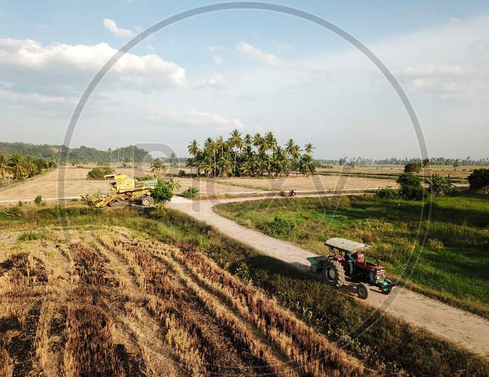 Tractor Move At Path In Paddy Field.Harvester Park At Background