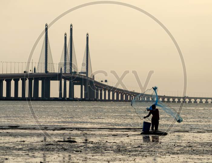 Fisherman Cast Net. Background Is Penang Second Bridge