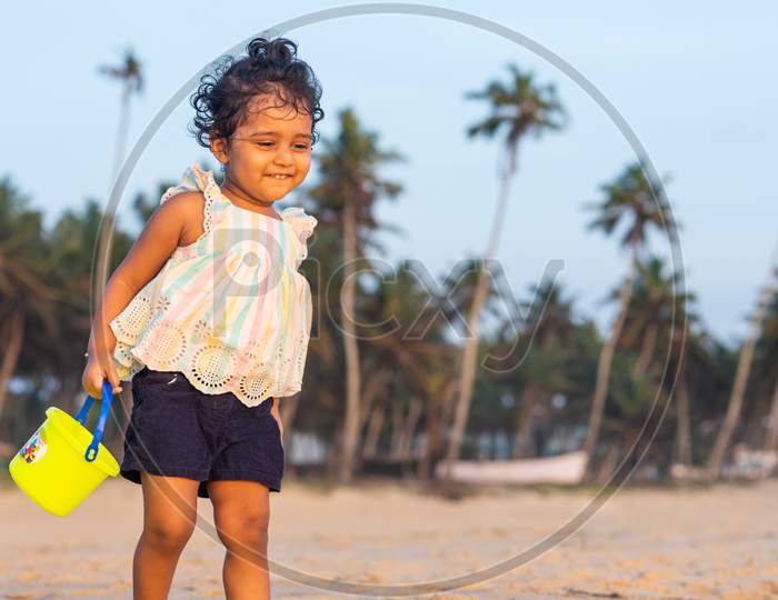 Playful Pretty Indian girl child/infant on the beach side playing with a sand kit and giving joyful expressions.
