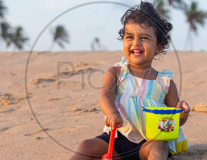 Playful Pretty Indian girl child/infant on the beach side playing with a sand kit and giving joyful expressions.
