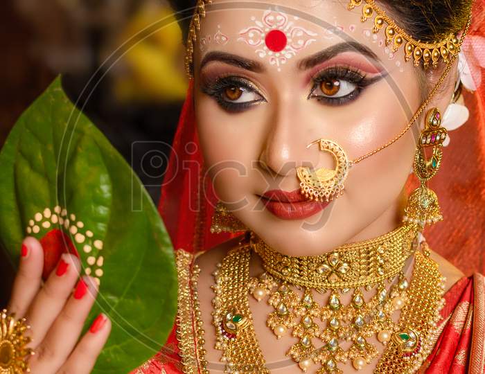 Portrait Of Very Beautiful Indian Bride Holding Betel Leaf, Bengali Bride In Traditional Wedding Saree And Makeup