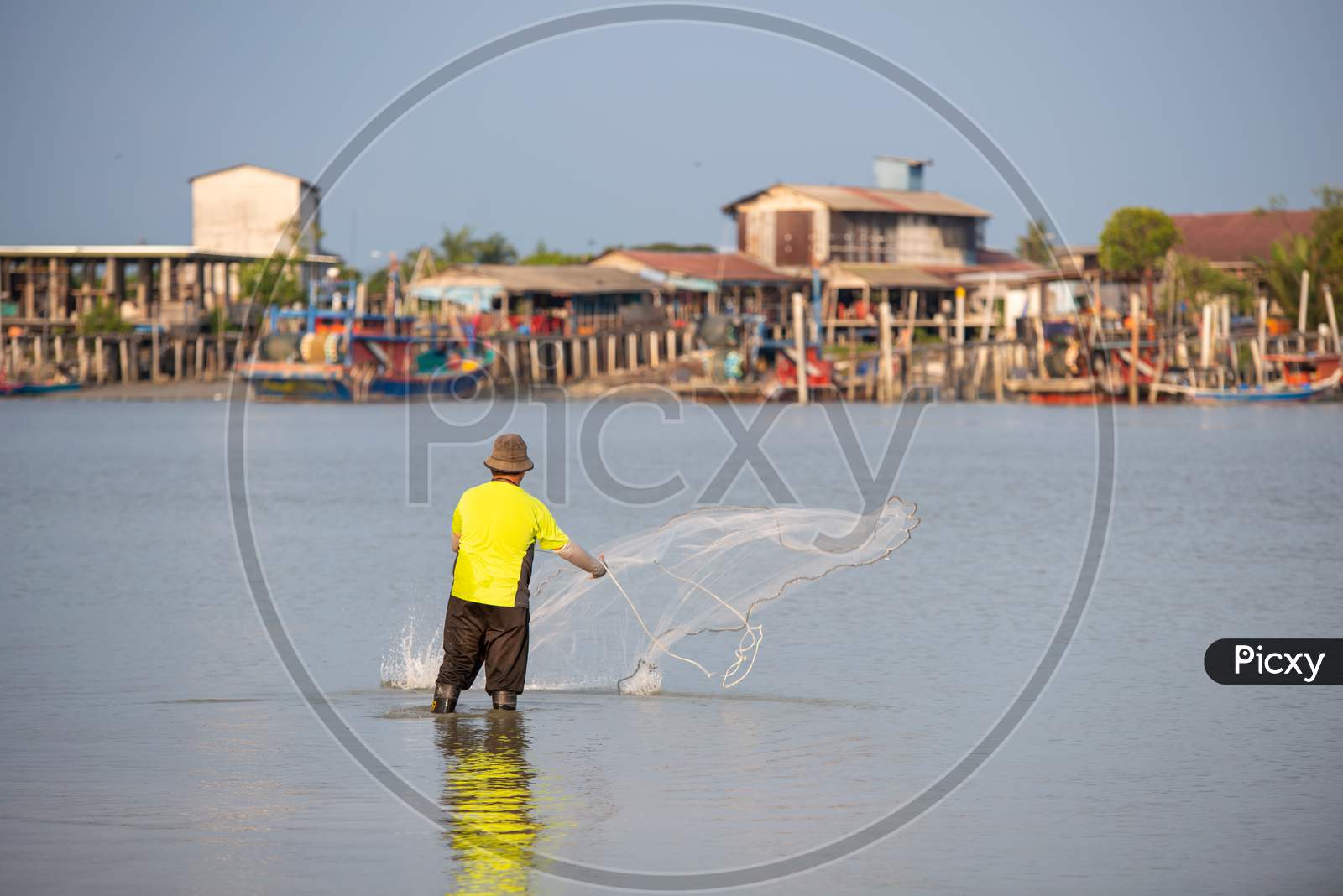 A Fisherman Throw The Net. Background Is Fishing Village
