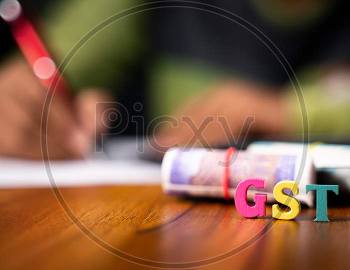 Selective Focus On Gst Letters, Concept Of Man In Background Doing Gst Or Goods And Service Tax Savings Calculation.