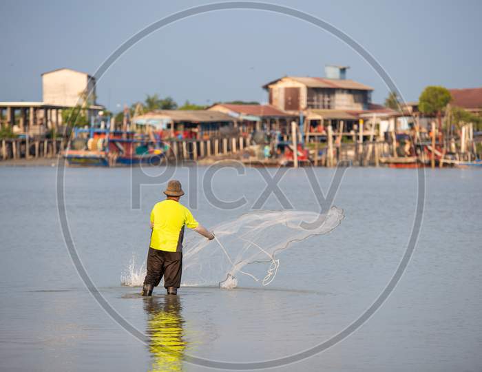 A Fisherman Throw The Net. Background Is Fishing Village