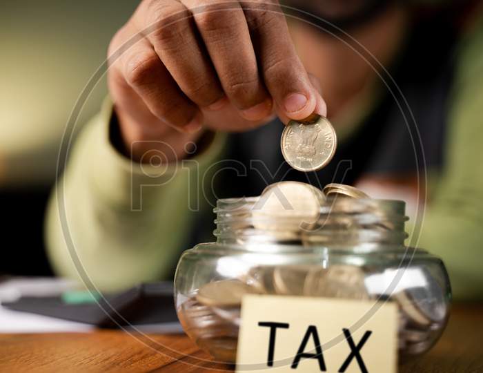Concept Of Tax Savings Selective Focus On Coins , Man Placing Coins Inside The Bowl With Tax Written On Bowl.
