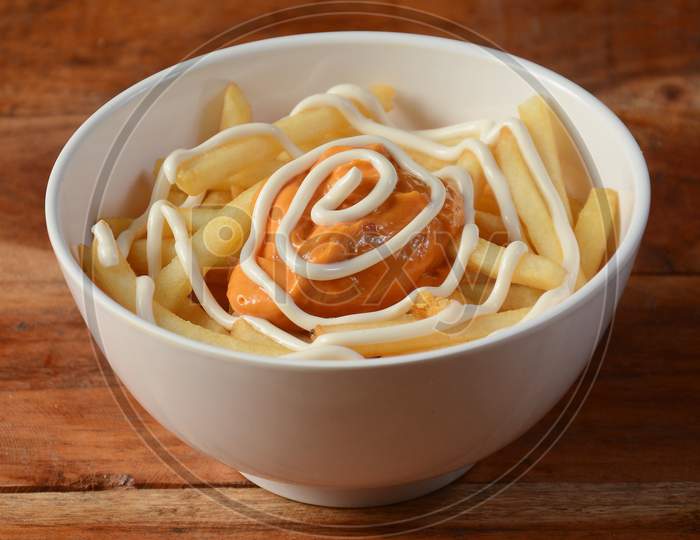 French Fries Topped With Chipotle Flavored Cheese, Served In A Bowl Over A Rustic Wooden Background, Selective Focus