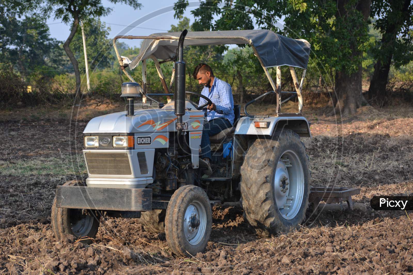 TIKAMGARH, MADHYA PRADESH, INDIA - NOVEMBER 24, 2020: Indian farmer with tractor preparing land for sowing with harrow.