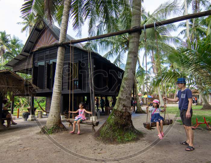 Children Play Swings In Front Of Wooden Malays Hut