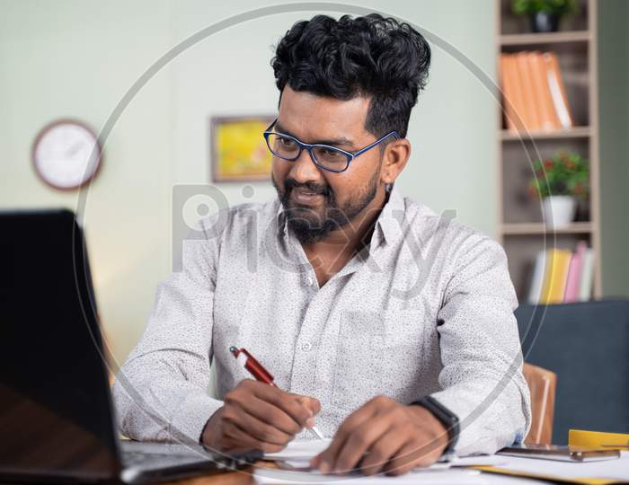Young Man Writing Down Notes By Looking Laptop - Concept Of Employee Or Student Online Training At Home.