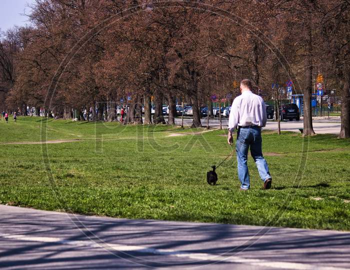 Krakow, Poland: A Man Walking His Pet Dog In The Open Blonia Park During Summer. Błonia Park Is A Vast Meadow With An Area Of 48 Hectares Directly Adjacent To The Historic Centre Of The City