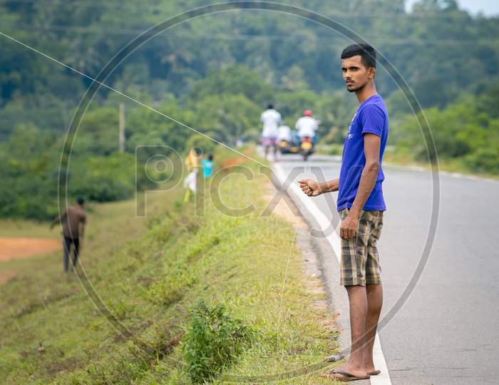 Young Teenage Boy Flying A Kite Holding The String In The Side Of A Road,