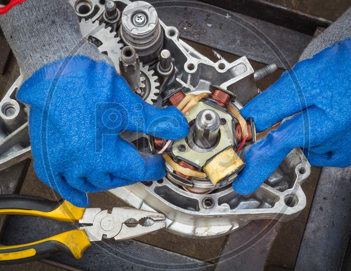 A Dexterous pair of hands is carefully assembling a Electrical stator coil plate inside a Motorcycle engine during an Overhauling procedure at Motorcycle workshop in Mysuru,India.