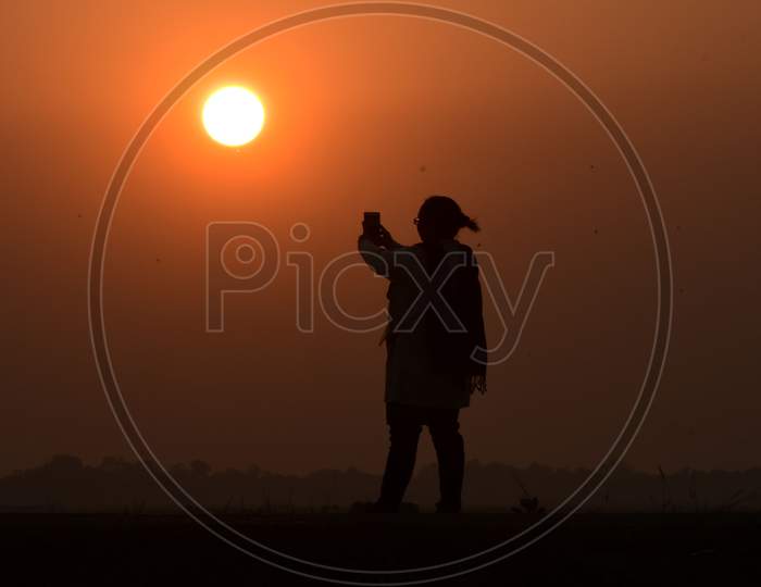 A girl try to capture  the last sunset of the year on her mobile phone  in Assam on Dec 31,2020.