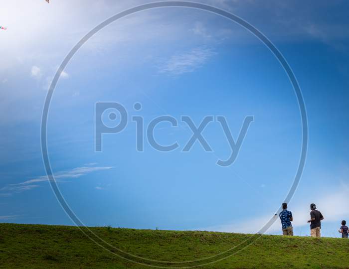 Two Boys Flying Kites In A Grassland Mountain Hill, Blue Bright Sky Scenic Landscape,