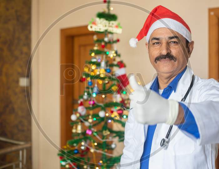 Middle Age Doctor Wearing Christmas Hat Doing Thumb Up, Happy Man Face Smiling. Celebration During Covid-19 Pandemic, Lockdown, Stay At Home, New Normal.