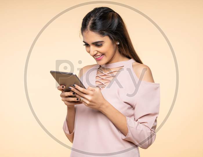 Indian excited young woman smiling while using Mobile Tab