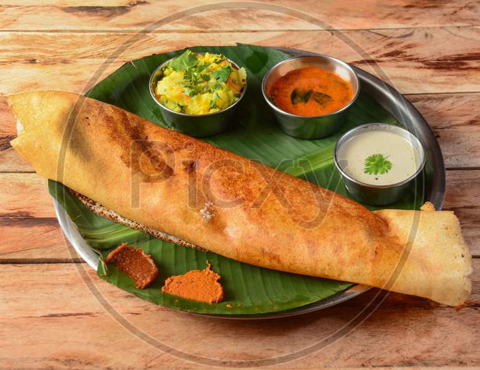 Masala Dosa, A South Indian Traditional And Popular Crepe With Filling Of A Mixture Of Mashed Potatoes And Fried Onions Served With Chutney And Sambar Over A Rustic Wooden Background, Selective Focus