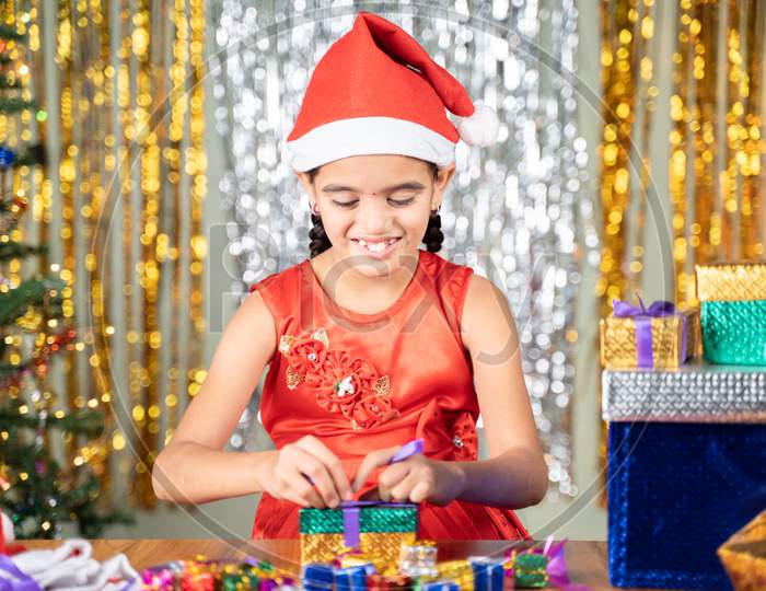 Happy Smiling Young Girl Kid With Santa Hat On Christmas Decorated Background Buys In Preparing Or Packing Gift Boxes For Holiday Celebration.
