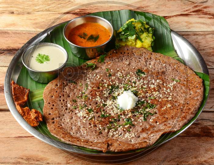 Ragi Dosa Or Finger Millet Dosa A South Indian Traditional Breakfast Served With Chutney,Sambar And Potato Masala Topped With Butter And Served Over A Rustic Wooden Background, Selective Focus