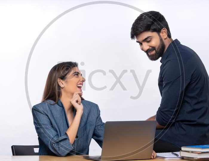 Indian male and female office colleagues smiling at each other