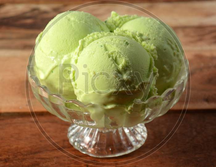 Pista Ice Cream Scoops Served In A Glass Bowl Over A Rustic Wooden Table, Selective Focus