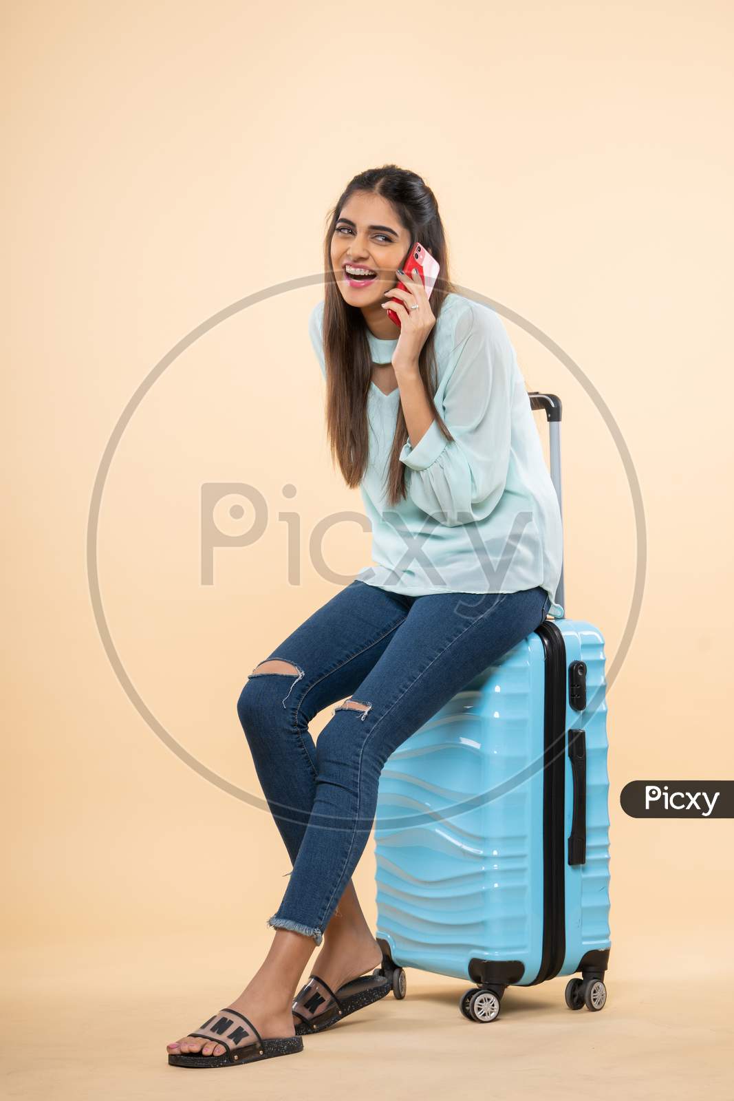 Indian young woman with  a travel trolley bag using mobile phone