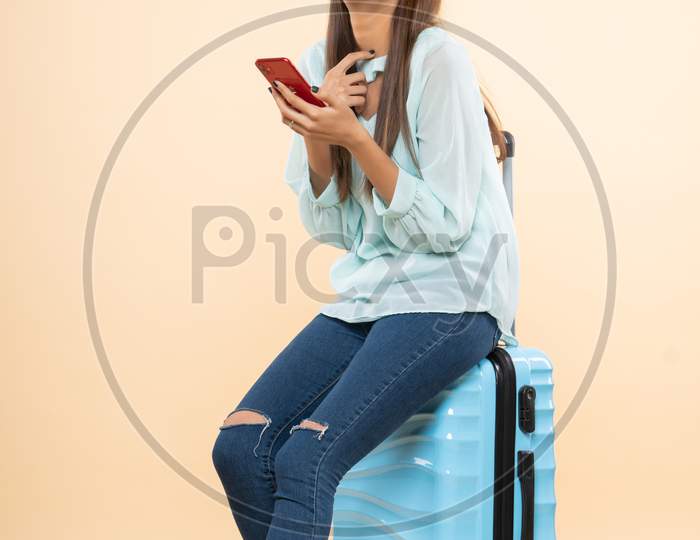 Indian young woman with  a travel trolley bag using mobile phone