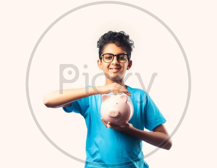 Cute Little Indian Asian Boy Holds Piggy Bank With Books Against White Background