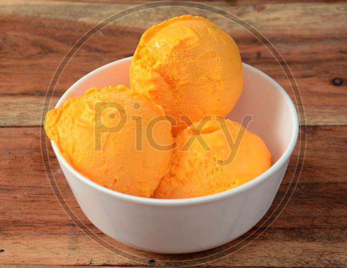 Mango Ice Cream Scoops Served In A White Bowl Over A Rustic Wooden Table, Selective Focus